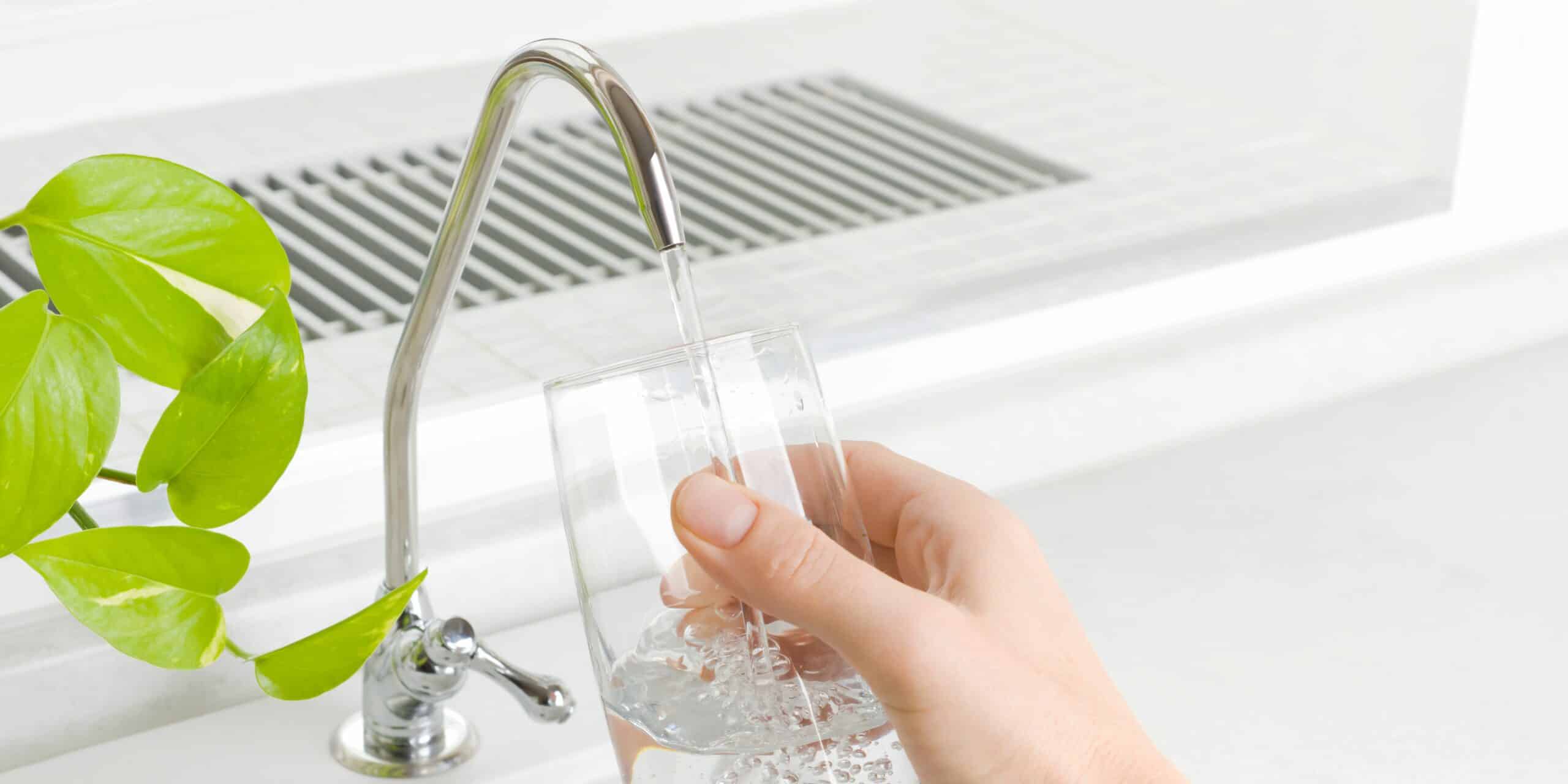 Hand holding a glass and filling it up with water from the faucet.